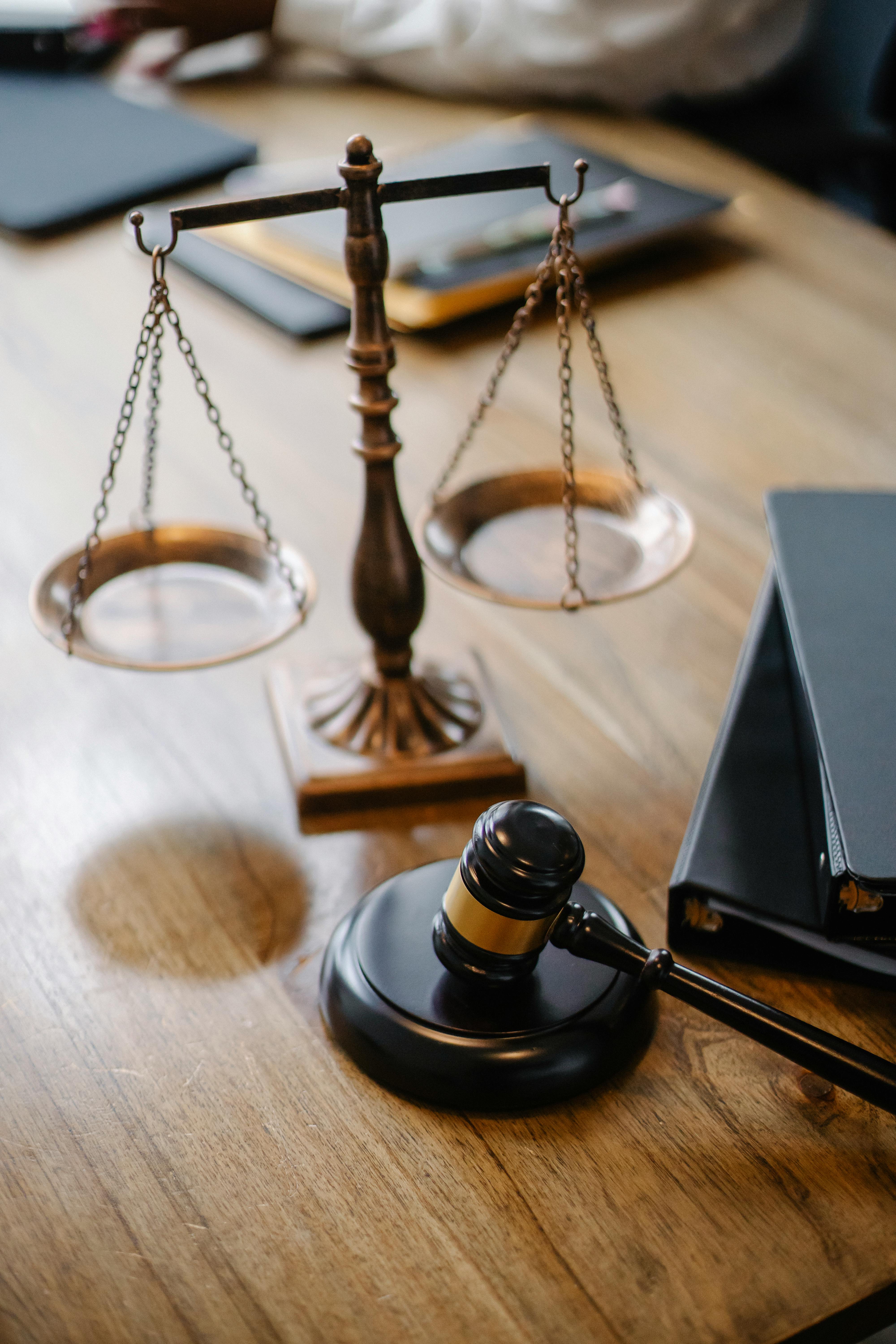 image of a justice balance scale and a gavel on a brown table with 2 black journals