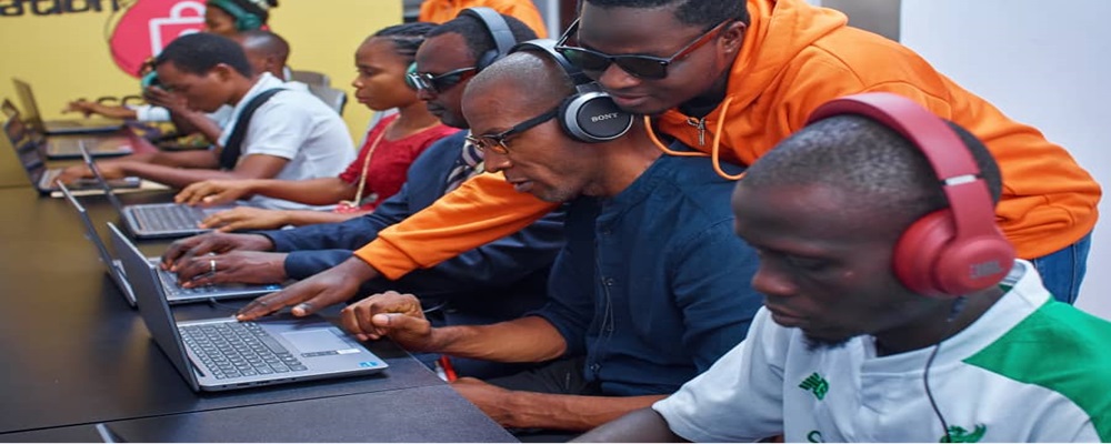 7 Visually impaired students seated using headsets and laptops on a table, with a tutor providing hands-on assistance.